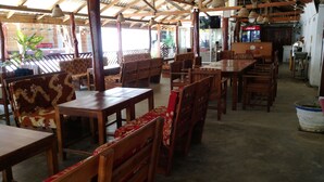 A restaurant with wooden tables and chairs, a Coca-Cola refrigerator, and a TV screen. - Hangloose Arugambay (Arugam Bay)