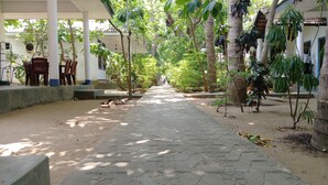 A covered walkway with stone flooring, surrounded by trees and plants, leading to a building with columns and a covered seating area. - Hangloose Arugambay (Arugam Bay)