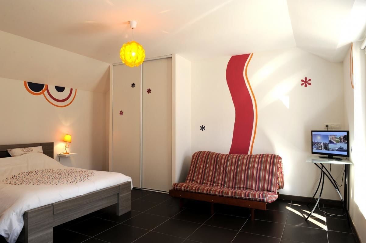 A bedroom with a bed, a sofa, a TV, and a door.