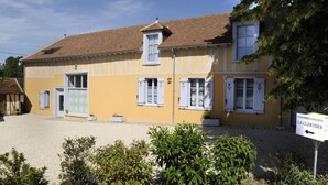 Um edifício amarelo com persianas brancas e uma placa que indica 'Chambres d'Hotes La Clérhier'.