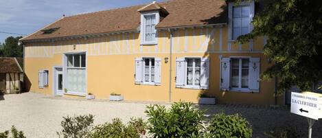 A yellow building with white shutters and a sign indicating 'Chambres d'Hotes La Clérhier'.