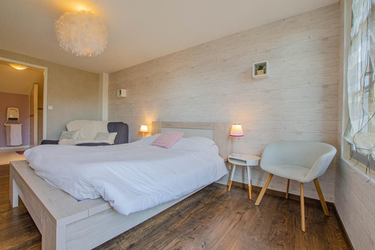 Ein Schlafzimmer mit einem großen Bett, Nachttischen mit Lampen, einem Sessel und Holzboden.
