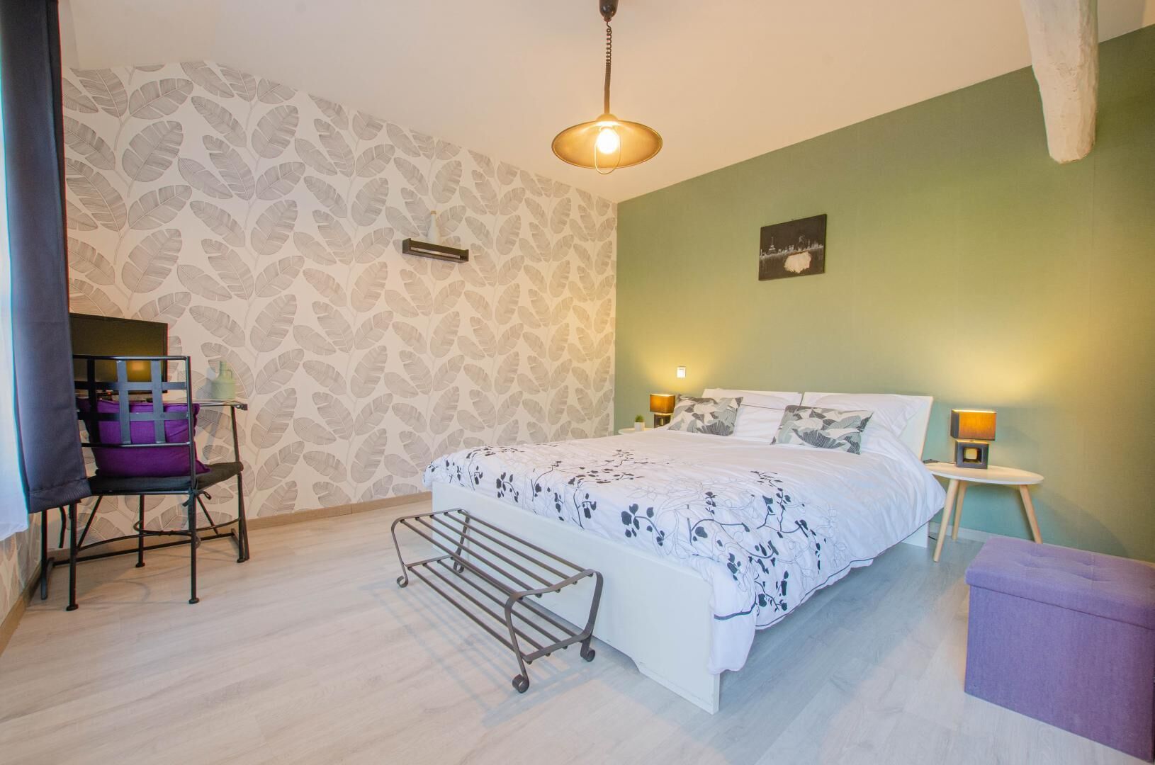 A bedroom with a bed, two bedside tables, a chair, a small table, and a wall with a leaf pattern.