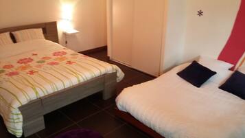 Een hotelkamer met twee bedden, waarvan één met een bloemenprint sprei en de ander met een effen witte sprei. Tussen de bedden staat een nachtkastje met een lamp.