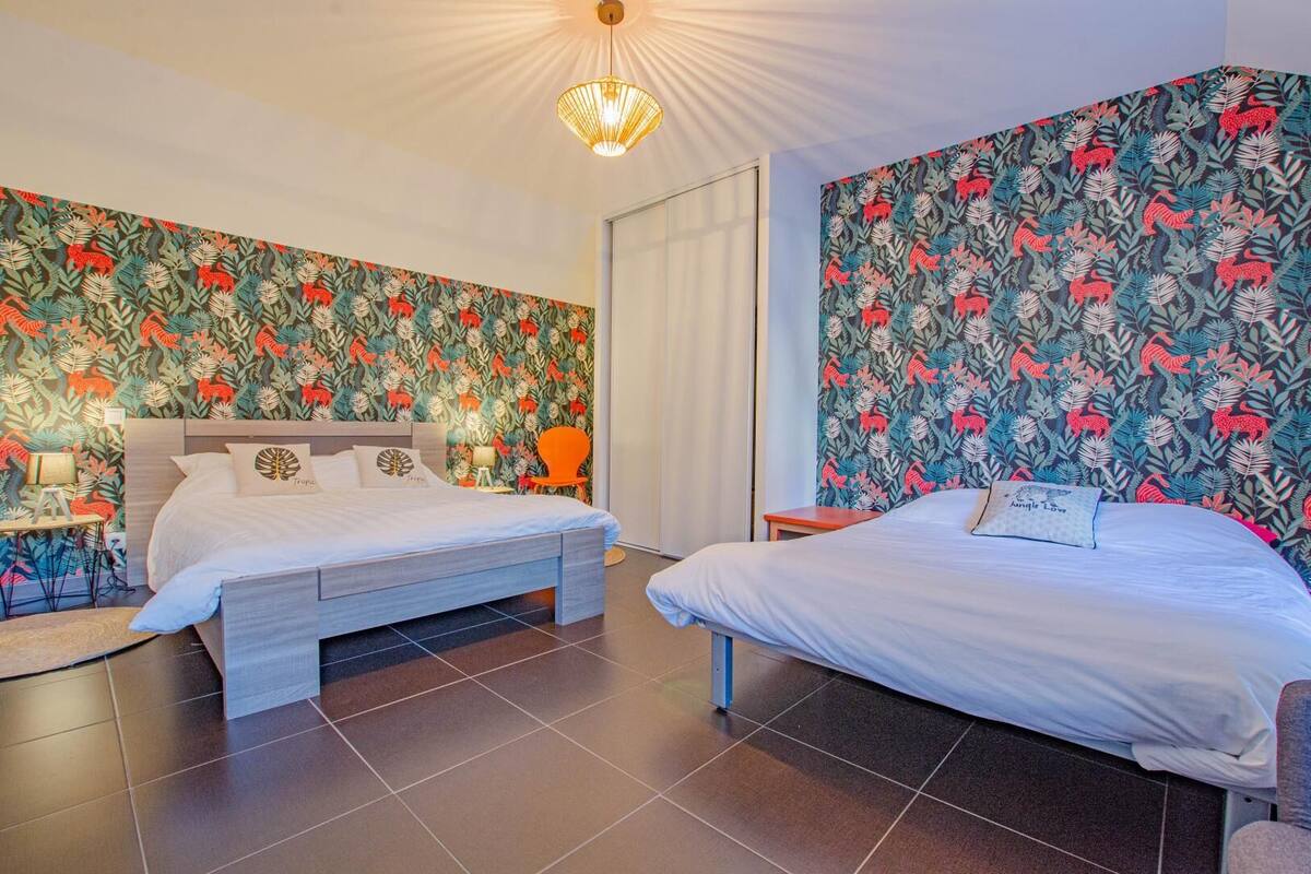 Ein Hotelzimmer mit zwei Betten, einem Nachttisch mit Lampe, einem Sessel und einem großen Fenster.