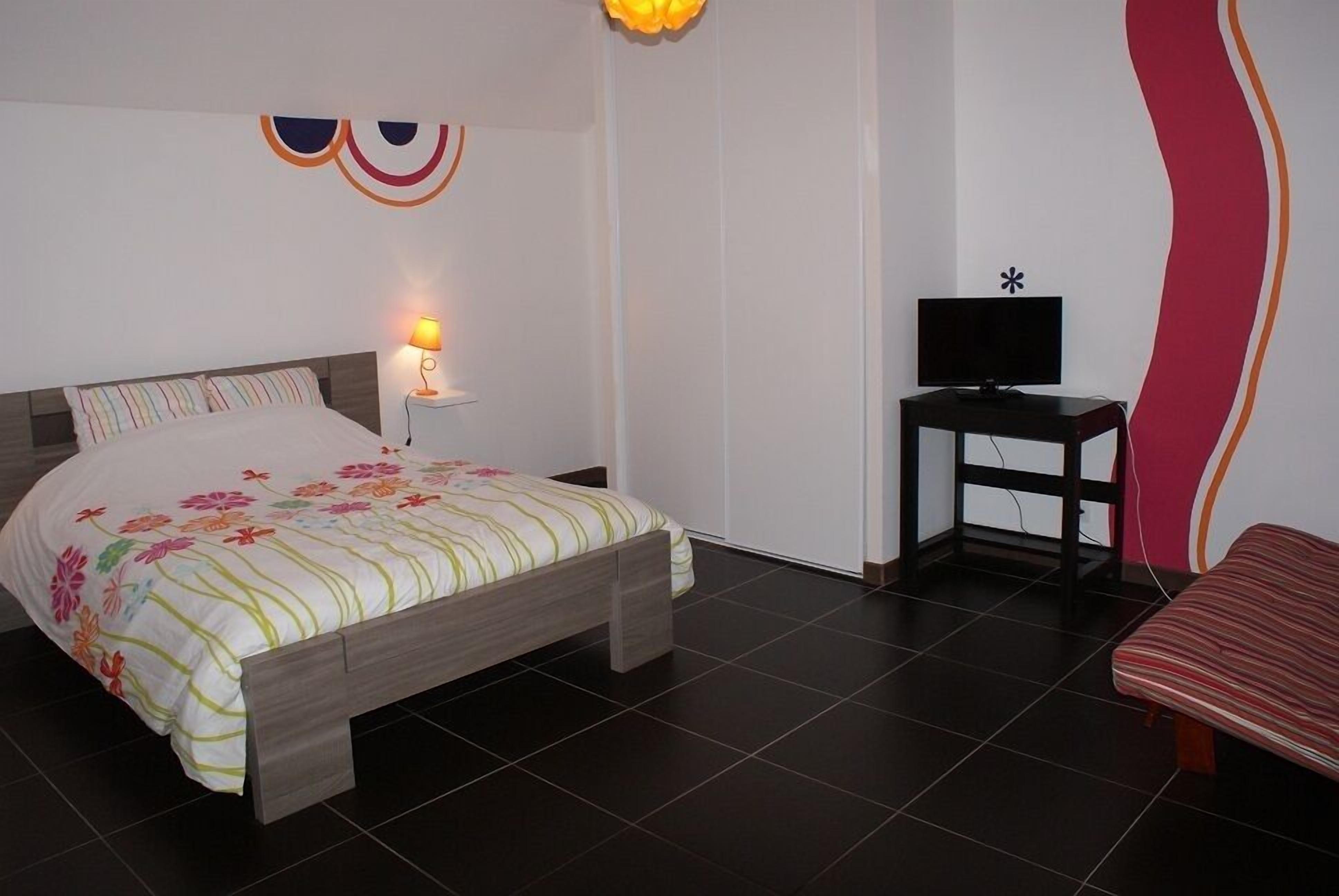 Ein Schlafzimmer mit einem Bett, einem Nachttisch mit Lampe, einem Fernseher auf einem Schrank und einem Sessel.