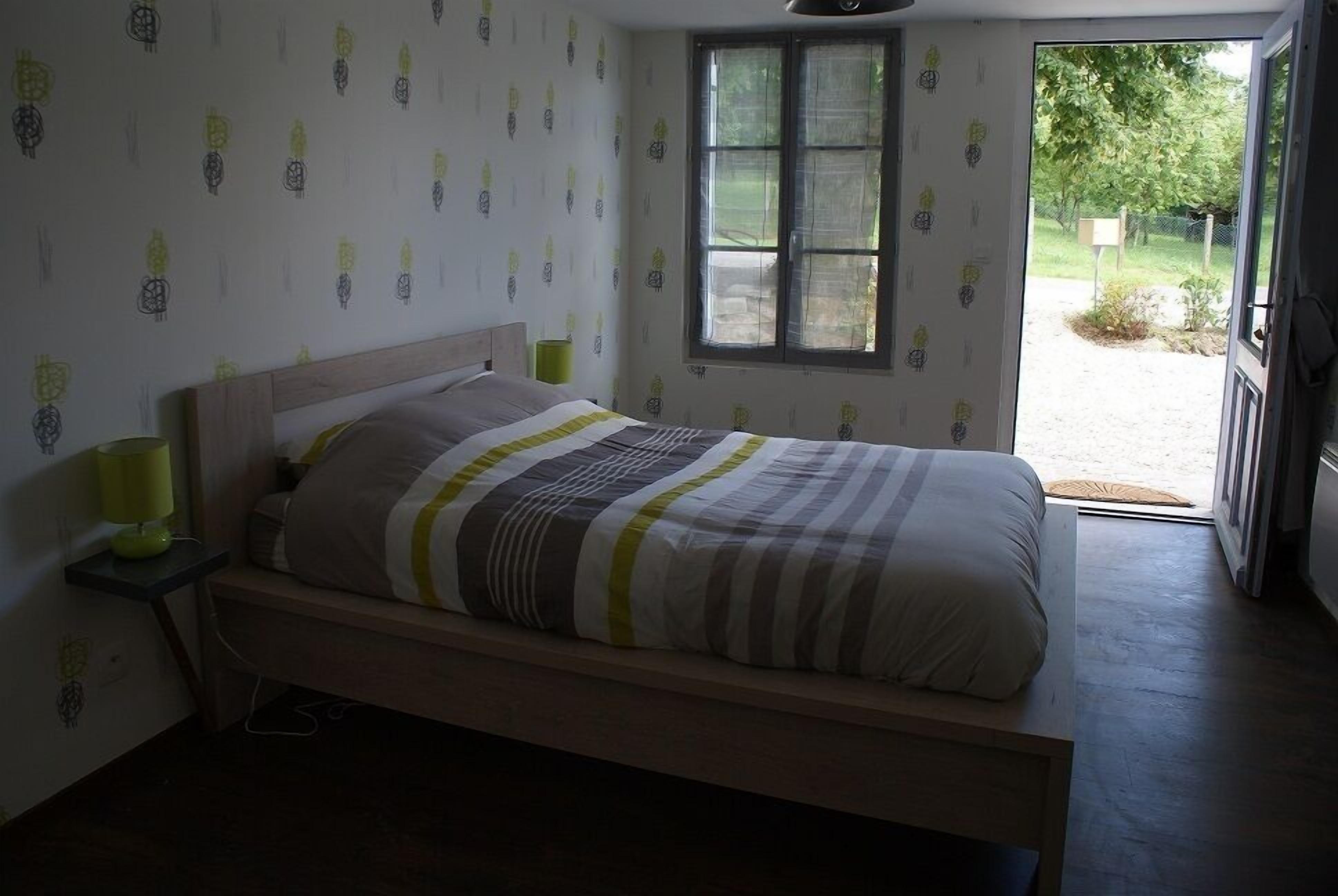 Un dormitorio con cama, lámparas de noche, ventana y puerta que da al exterior.