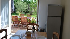 Puerta abierta que da a un patio con mesa lista para comer, sillas de madera y un refrigerador.