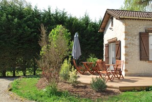 Ein rustikales Haus mit einer Holzterrasse, einem kleinen Tisch und Stühlen sowie einer überdachten Sitzgelegenheit im Freien.