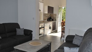 Una sala moderna con sofás oscuros, una mesa de centro y una cocina al fondo.