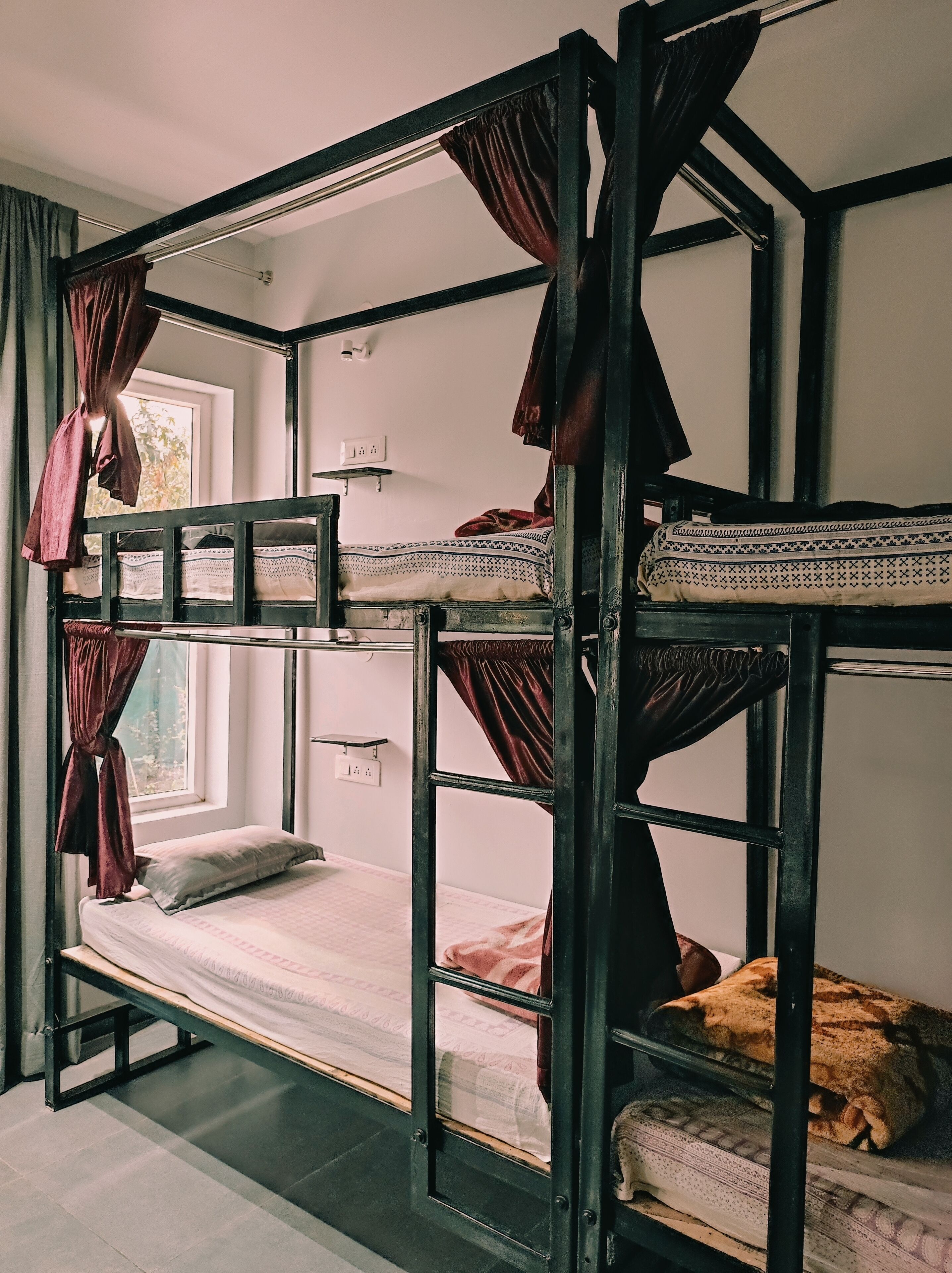 A bunk bed room with a window, curtains, and a shelf with a light fixture.