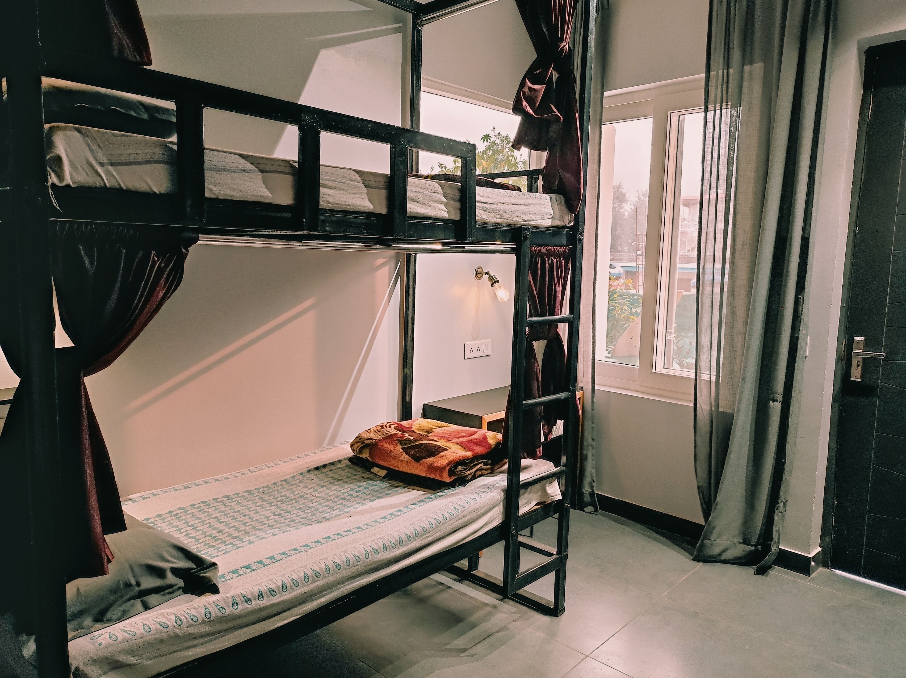A bunk bed room with a ladder, a window with curtains, and a door.