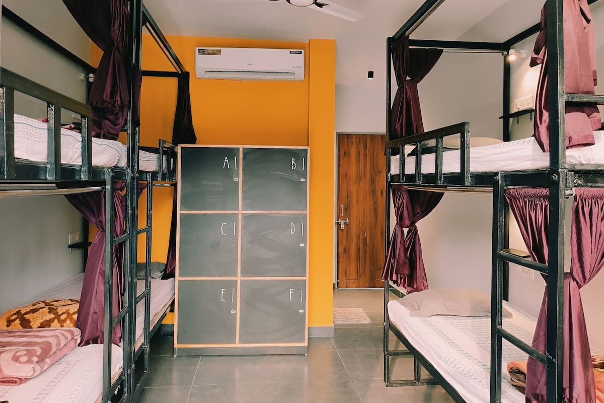 A dormitory room with bunk beds, a chalkboard with letters, an air conditioning unit, and a ceiling fan.