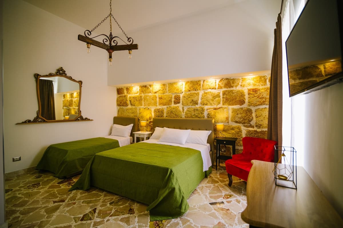 Ein Hotelzimmer mit zwei Betten, einer Steinwand, einem hölzernen Kopfteil, einem roten Sessel, einem kleinen Tisch und einem Fernseher.