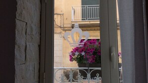 Blick durch ein Fenster mit einem Metallgitter, ein Balkon mit einem grünen Rollo und ein Gebäude mit einer gelben Fassade.