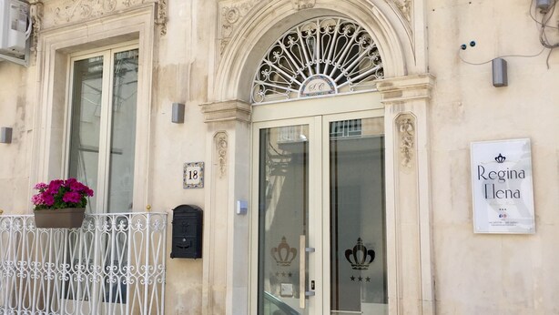 Ein Gebäude mit aufwendigen architektonischen Details, darunter ein dekorativer Eingangsbereich mit Glastür und ein Balkon mit einem Blumentopf.