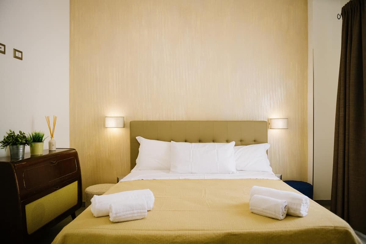 Ein Hotelzimmer mit einem Bett, Nachttischlampen, einem Nachttisch mit Lampe und einem kleinen Tisch mit Pflanze.