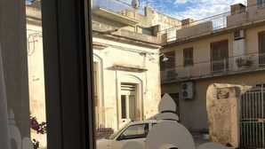 Blick durch ein Fenster mit dekorativem Rahmen, ein weißes Auto vor der Tür und ein Gebäude mit Balkonen und Satellitenschüsseln.
