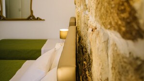 Ein Hotelzimmer mit einer Wand aus Stein, einem Bett mit grüner Bettwäsche, einem Spiegel und Einbauleuchten.