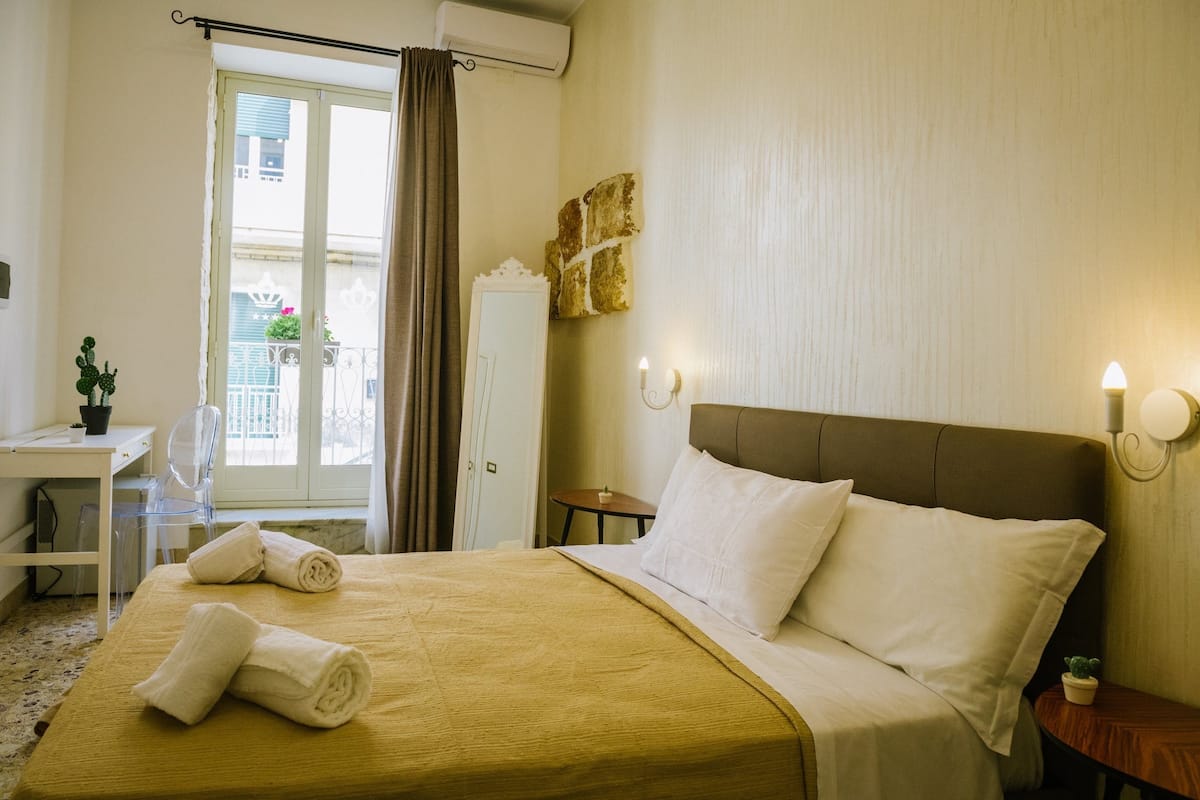 Ein Hotelzimmer mit einem Bett, einem Schreibtisch, einem Sessel, einem kleinen Tisch und einer Topfpflanze.