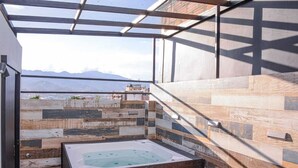A modern bathroom with a large bathtub, a bench, and a view of mountains. - 3 BEDROOM PENTHOUSE MIDDLE OF PARK LLERAS PRIVATE ROOF TOP WITH HOT TUB AC (Medellin)
