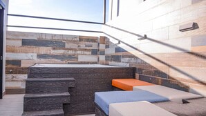 A modern bathroom with a stone wall, a bathtub, and a set of steps leading to a seating area with cushions. - 3 BEDROOM PENTHOUSE MIDDLE OF PARK LLERAS PRIVATE ROOF TOP WITH HOT TUB AC (Medellin)
