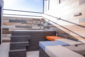 A modern bathroom with a stone wall, a bathtub, and a set of steps leading to a seating area with cushions.