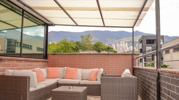 An outdoor patio with wicker furniture, a glass wall, and a view of distant mountains. - Lower Penthouse Two Bedroom AC DECK with Hot Tub Elevator AC (medellin)