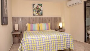 A hotel room with a bed, two bedside tables, a nightstand, a wall-mounted air conditioner, and a painting above the bed. - Lower Penthouse Two Bedroom AC DECK with Hot Tub Elevator AC (medellin)