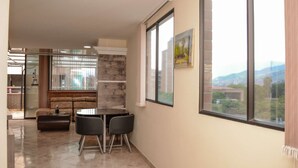 A modern living room with a sofa, a coffee table, and two chairs. There is a large window with a view of buildings and mountains. - Lower Penthouse Two Bedroom AC DECK with Hot Tub Elevator AC (medellin)