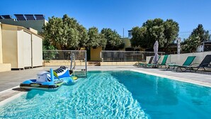 A swimming pool with a blue inflatable boat, sun loungers, and a fence.