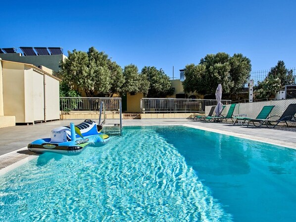 A swimming pool with a blue inflatable boat, sun loungers, and a fence.