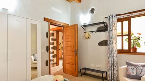 A cozy room with a bed, a wooden door, a small table with snacks, a window with a plant, and a white sofa.