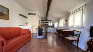 Un soggiorno con un divano rosso, una zona pranzo con sedie in legno, una cucina con mobili bianchi e un pavimento piastrellato.