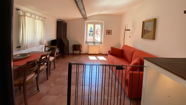 Un soggiorno con un divano rosso, mobili in legno, pavimento piastrellato e una finestra con tende.