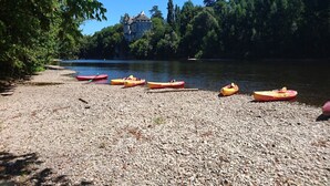 A gravel beach with kayaks lined up, a castle in the background, and dense trees around a lake.