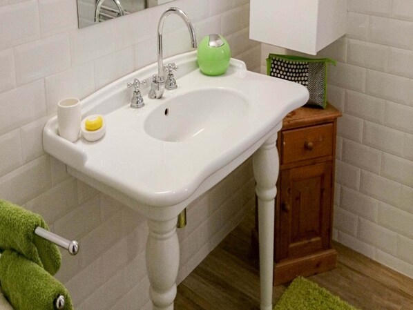 Un baño con un lavamanos blanco, dos grifos, un dispensador de jabón verde y un pequeño armario de madera.