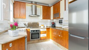 A modern kitchen with wooden cabinets, stainless steel appliances, and a granite countertop. - Beautiful penthouse in the heart of Alicante (Alacant)