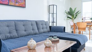 A modern living room with a blue sofa, checkered pillows, a wooden coffee table with decorative vases, and a colorful abstract painting on the wall. - Beautiful penthouse in the heart of Alicante (Alacant)