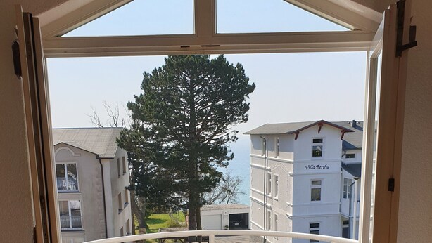 Varanda com mesa e duas cadeiras, deck de madeira e vista para edifícios vizinhos.