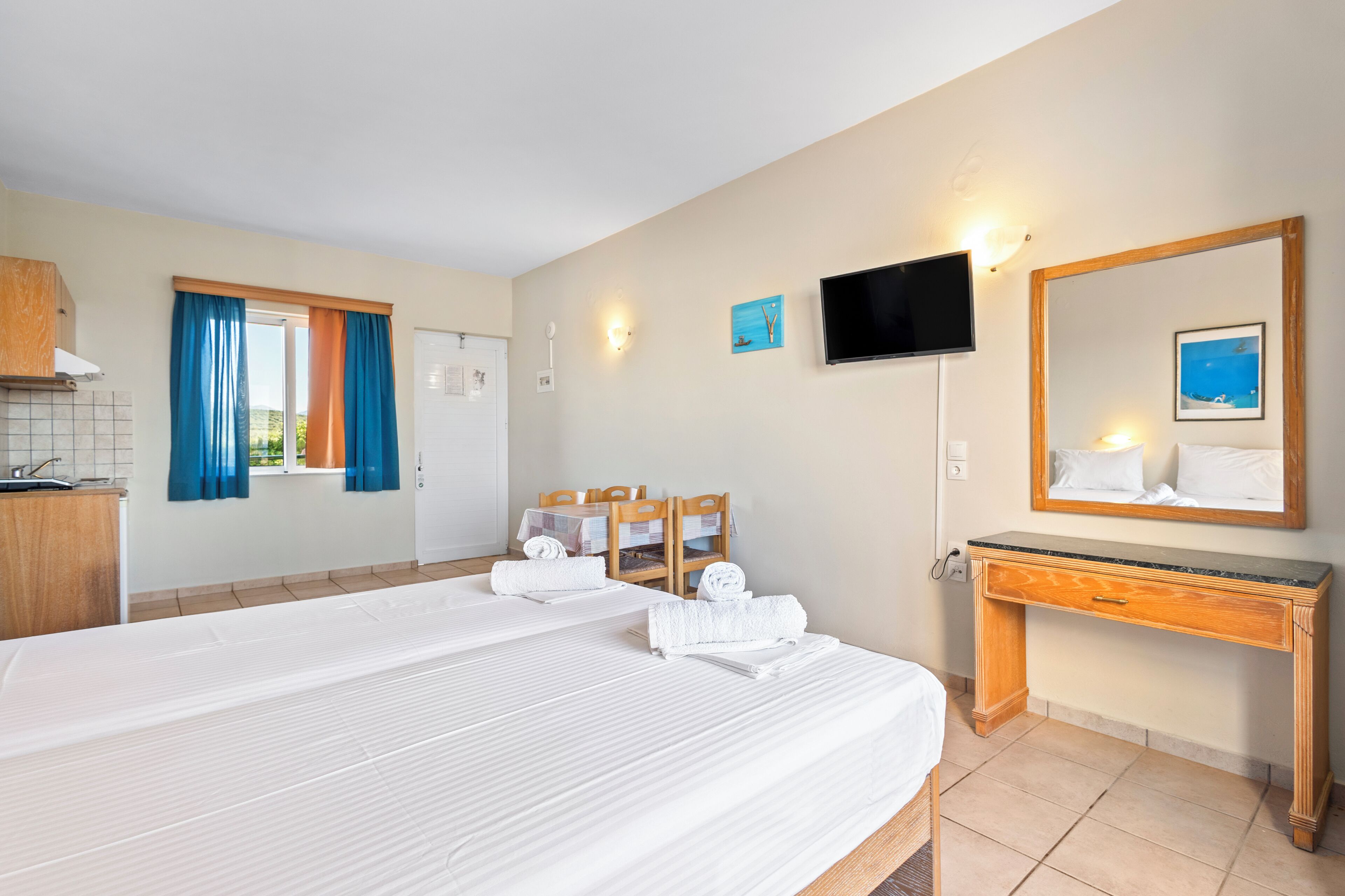 A hotel room with two beds, a TV, a mirror, a wooden desk, and a small table with chairs.