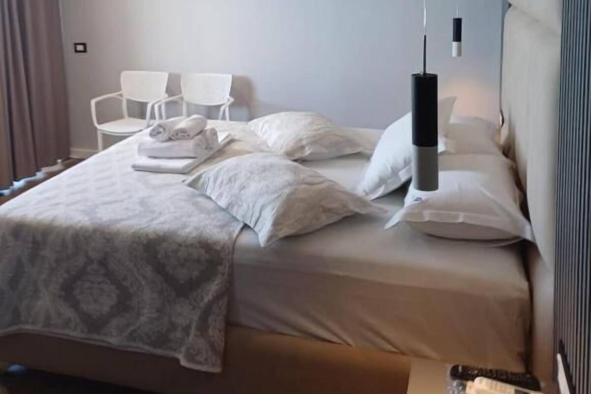 Ein modernes Hotelzimmer mit einem ordentlich bezogenen Bett, einem Nachttisch mit Fernbedienung und einer Pendelleuchte.