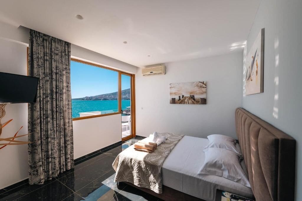 Una camera da letto con un'ampia finestra, un letto, una televisione a schermo piatto e un quadro appeso al muro.