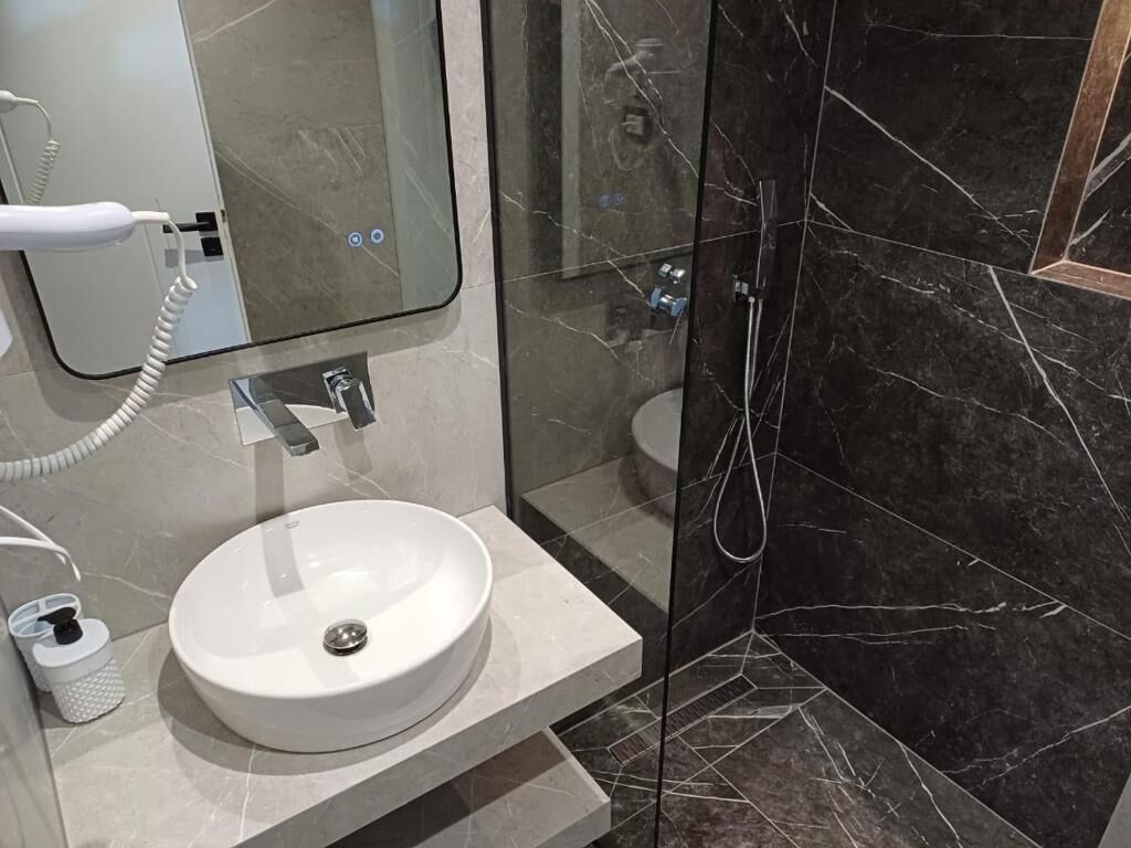 A bathroom with a white sink, a glass shower enclosure, and a marble-tiled shower wall.