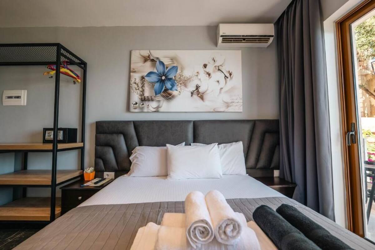Ein Hotelzimmer mit Bett, Wandklimaanlage, großem Fenster mit Vorhängen und einem Gemälde über dem Bett.