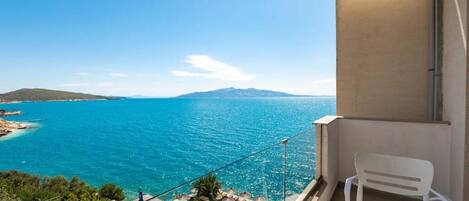 A balcony with a clear view of the sea, a white chair, and a glass table.