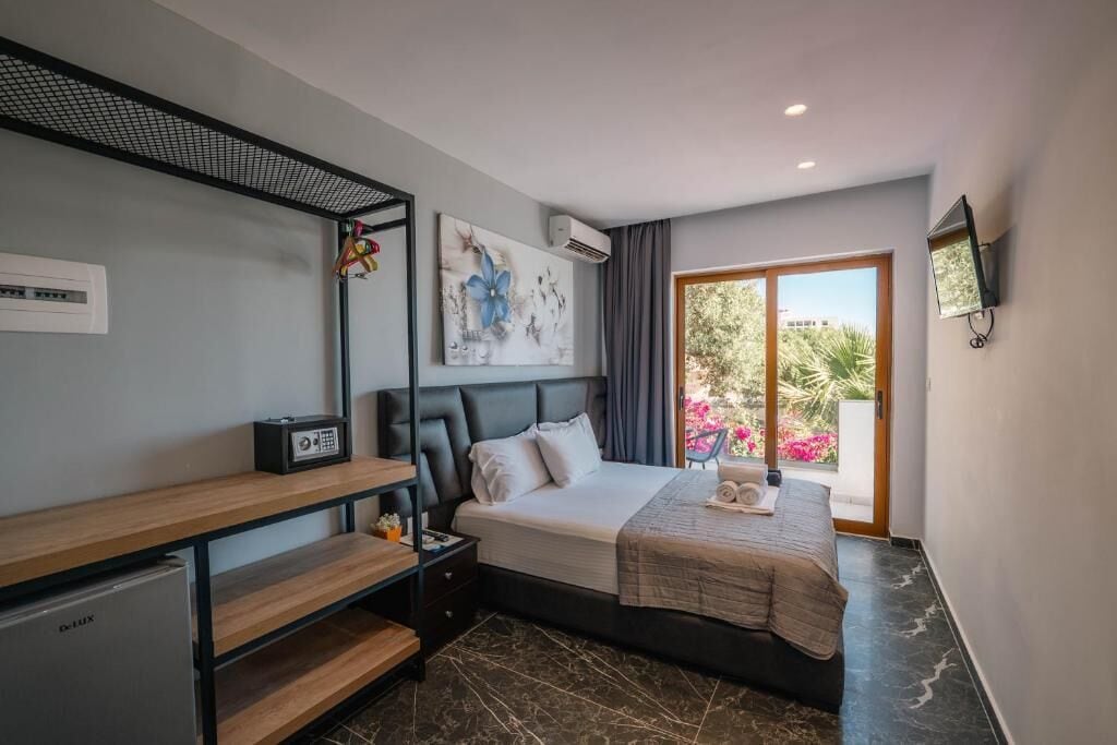 A modern hotel room with a bed, a desk, a chair, a TV, and a balcony with a view of the outdoors.