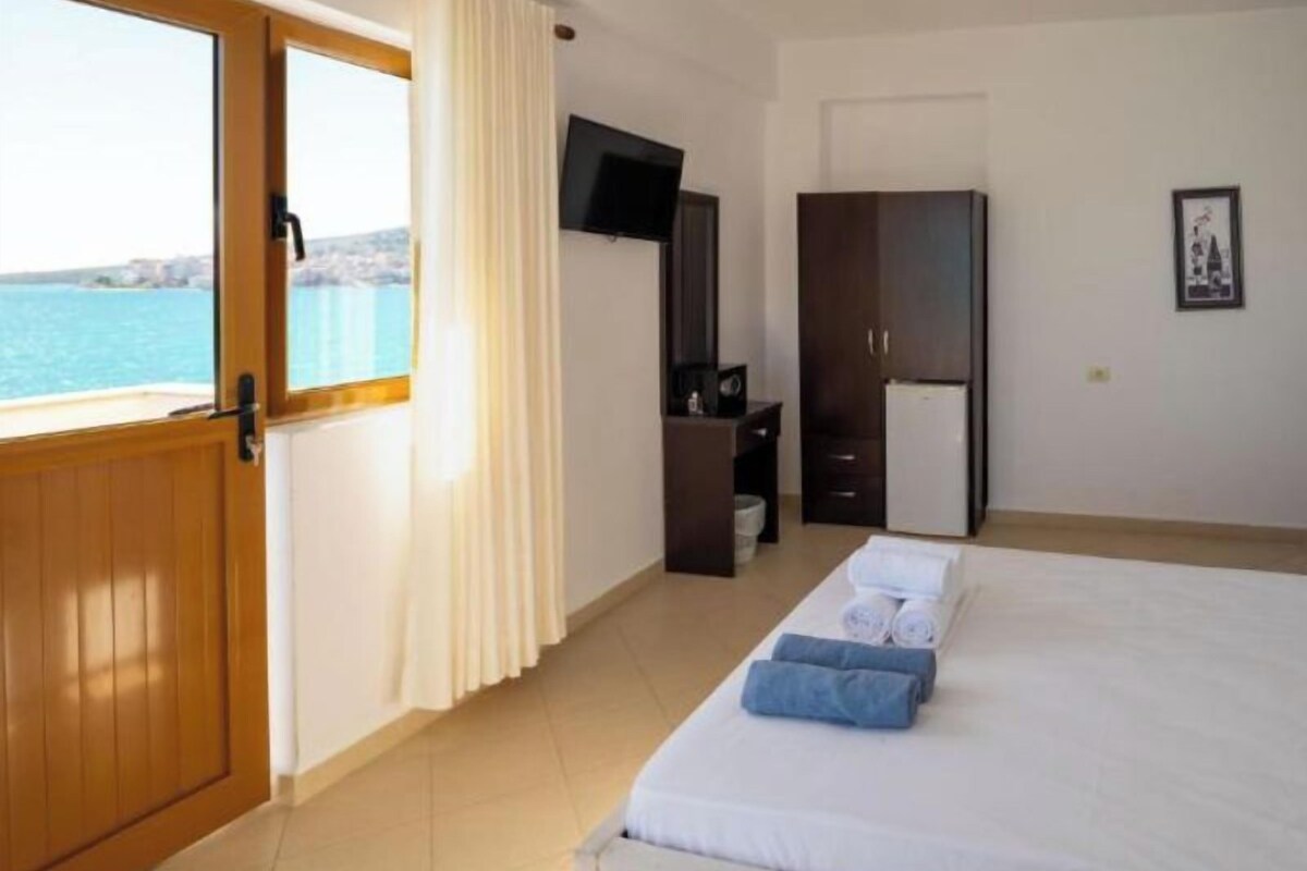 A hotel room with a bed, a TV, a wardrobe, and a view of the sea.