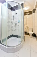 Ducha con cerramiento de vidrio, cabezal de ducha de mano y grifo empotrado en la pared.