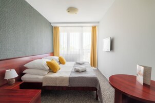 Habitación de hotel con cama, mesita de noche, lámpara, televisor y una mesa con una tarjeta de menú.